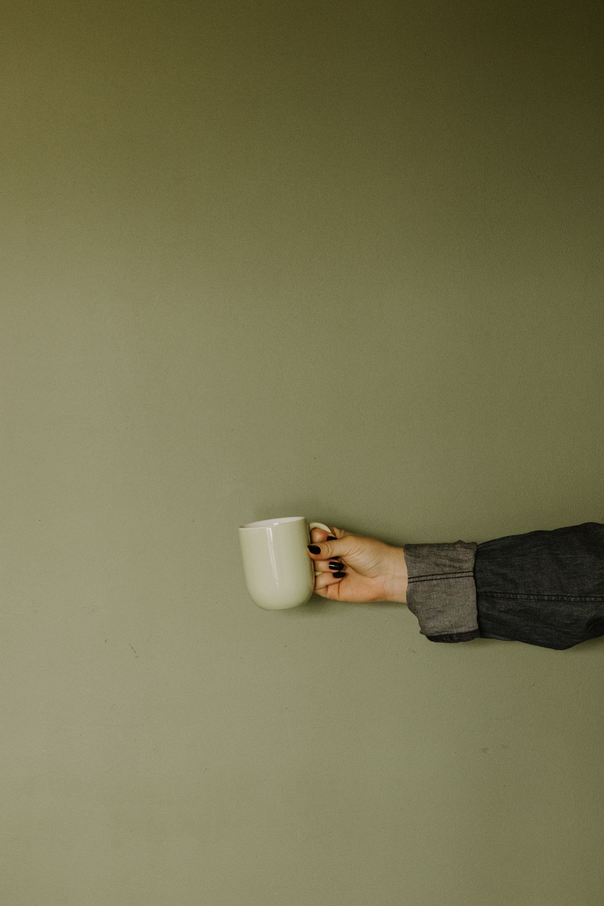 Una mano sostiene una taza de cerámica delante de una pared verde.